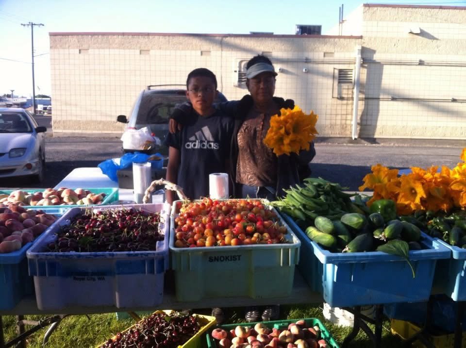 Isaías de niño junto a su abuela en el puesto de fruta de la familia, con cajas de cerezas y duraznos al frente.